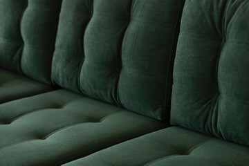 Soft vintage sofa in green velor with a quilted seat and a back of stitched cushions. Part of stylish furniture covered with plush fabric in emerald color close-up. - obrazy, fototapety, plakaty