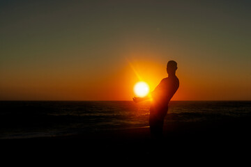 Krajobraz morski, sylwetka człowieka podnosząca słońce. Zachód słońca na plaży. 