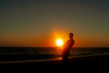 Krajobraz morski, sylwetka człowieka podnosząca słońce. Zachód słońca na plaży. 
