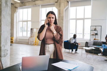 Nervous lady having phone conversation in workspace