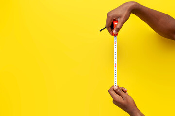 hands of african american man hold tape measure on yellow isolated background, hands measure the...
