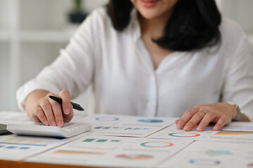 Close up image of businesswoman hand counting a numbers while Analyze graphs, diagrams and figures of financial document on office desk.