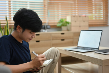 Portrait of young asian man doing homework while studying online with laptop at home.