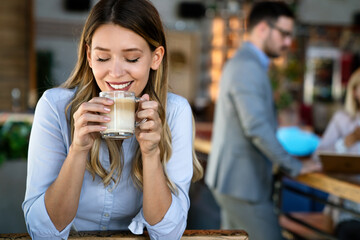 Portrait of happy young business woman drinking coffee in a break. In the background, her colleagues