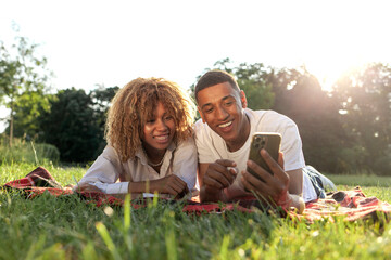 african american young couple lies in the park in the summer and uses smartphone