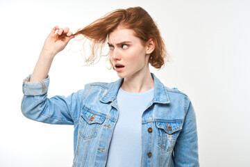 Portrait redhead young woman touching hair with displeased face isolated on white studio background, damaged hair concept