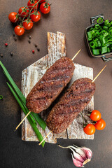 grilled lula kebab on skewers with spices on a wooden board, vertical image. top view. place for...
