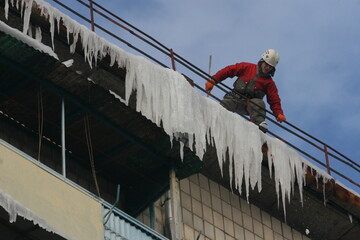 Ukraine, Kyiv - December 26, 2012: A worker knocks icicles off the roof of an apartment building. A man cleans the roof of ice.