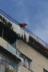 Ukraine, Kyiv - December 26, 2012: A worker knocks icicles off the roof of an apartment building. A man cleans the roof of ice.