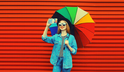 Portrait of happy smiling young woman taking selfie with phone with colorful umbrella on red...