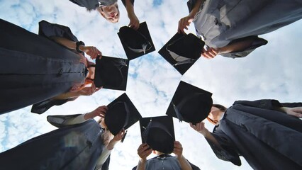 Joyful graduates stand in a circle and toss their caps up.