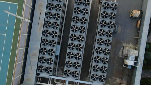 Three rows of outdoor air conditioner chiller fan coil compressors on the roof of a building. View from a drone