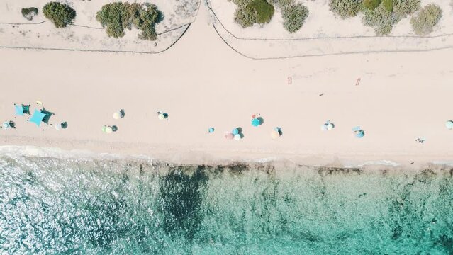 vista aerea top-down della spiaggia con gli ombrelloni colorati e il mare blu cristallino in estate. Spiaggia della Riserva naturale Salina Dei Monaci - Salento, Puglia, Taranto, Italia