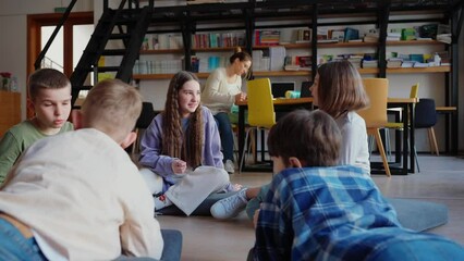 Pensive children talking in class while sitting in circle and teacher writing in notebook at library