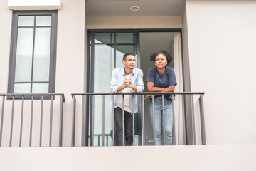 An Asian husband stands on the porch talking to his African American wife, planning to buy a new home together.