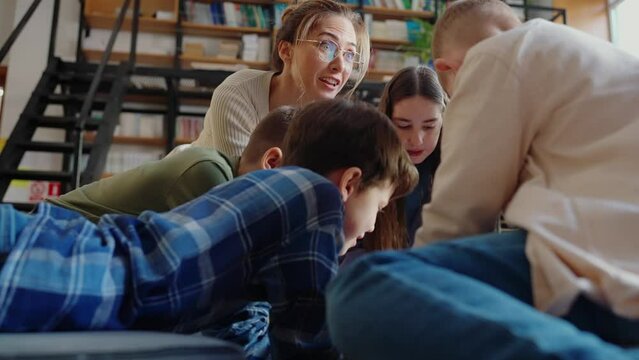 Surprised children and their teacher look at map of world sitting on floor in library 