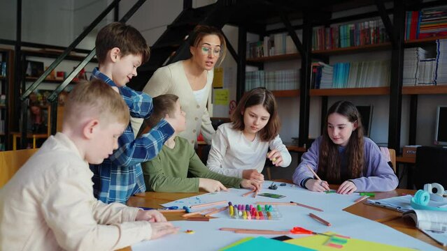 Positive teacher looks at drawings and plasticine figures that children have made at library