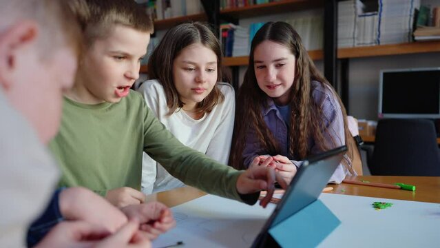 Handsome teenage boys and girls watching video on tablet at drawing table at library