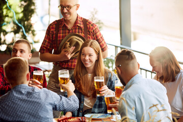 Group of cheerful young people, friends meeting at cafe, pub, spending time together, drinking beer. Celebration and fun. Concept pktoberfest, traditional taste, friendship, leisure time, enjoyment