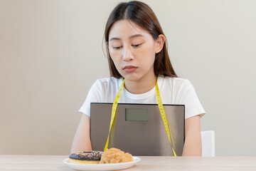 Diet, attractive asian young woman, girl restrained to eat doughnut, bakery and fried chicken, fast food to lose, loss weight, hugging weight scales on table at home. Passion, temptation when hungry.