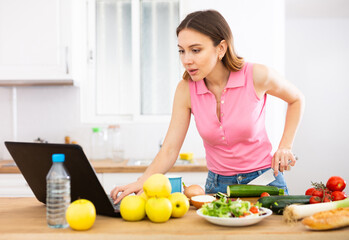 Young woman cooking vegetables for dinner and browsing sns on laptop