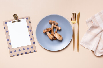 Mushrooms on a plate with cutlery and blank note on beige background flat lay, top view