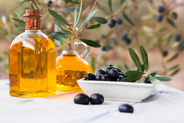 Black ripe olives, olive oil in a glass traditional bottle on table in an olive garden