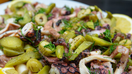 Boiled octopus salad is served with pure olive oil, lemon slices, dill, green olives and pickled cucumbers.  fresh and healthy seafood salad. Mediterranean gourmet appetizer.