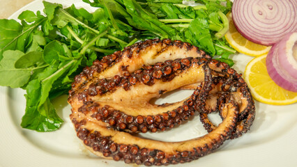 Octopuses, which have just come out of the Aegean Sea, are cooked on the grill fire and served on the plate with arugula, oregano, lemon and onions. Gokceada, Imbros island, Canakkale, Turkey