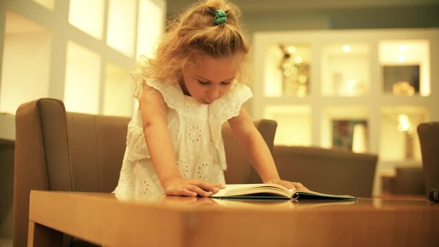 Little girl wearing a white dress reads a book