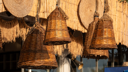 Stylish wicker chandeliers hanging in front of a bamboo garden wall © Arda ALTAY