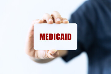 Medicaid text on blank business card being held by a woman's hand with blurred background. Business concept about medicaid.
