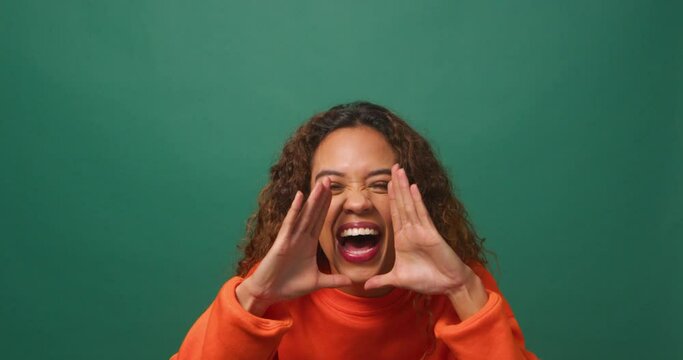 Young biracial woman raises hands, yells excitedly, green background studio