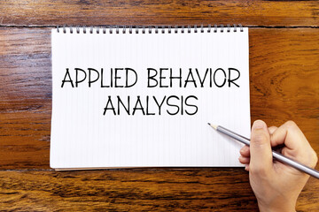 Applied behavior analysis handwriting text on blank notebook paper on wooden table with hand holding pencil. Business concept and legal concept about applied behavior analysis.
