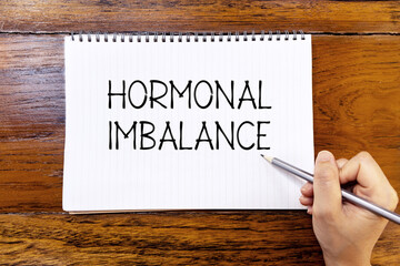 Hormonal imbalance handwriting text on blank notebook paper on wooden table with hand holding...