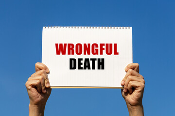 Wrongful death text on notebook paper held by 2 hands with isolated blue sky background. This...