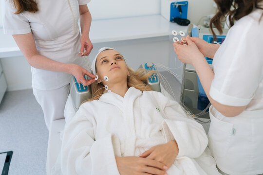 Cropped shot hands of two unrecognizable cosmetologists applying electrodes of myostimulator to woman face during bioresonance therapy in clinic of aesthetic medicine. Concept of rejuvenating skin