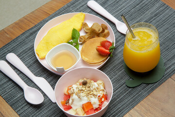 Kids menu - omlet, pancakes with maple syrup, muesli with yoghurt and glass of fresh squuzed orange juice served on the restaurant table with plastic kids friendly eating utensil. - obrazy, fototapety, plakaty