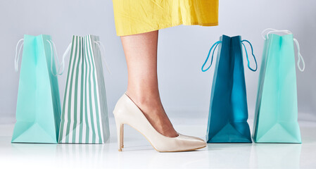 Shopping bag, shoes and a woman in studio for fashion sale, promotion or retail discount. Feet of a female model or customer on a white background advertising commerce offer, high heels or gift