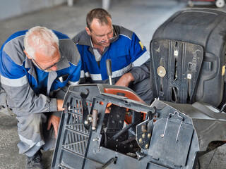 Two mechanics are repairing appliances in garage. Professional car mechanics repair garden tractor...