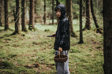 A boy with a wicker basket in his mouth. A child picks mushrooms alone in the forest. Soft selective focus