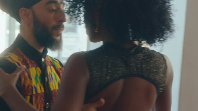 Attractive African-American woman in stage dress dancing sensual Argentine tango with male partner during rehearsal at studio