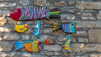 Colorful wooden fish ornaments on the stone wall. Modern Wood Art. Handmade carved from wood