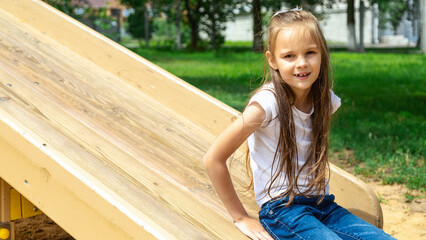 A cute little girl is playing in the children's yard. little kid sliding down from hill at playground