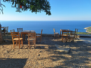 Fototapeta na wymiar Gokceada (Imbros) coastline and a cute village tea garden view with wooden chairs and table. Tepeköy village, Çınaraltı-Pinarbasi location, Aegean Turkey