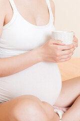 pregnant young woman sitting on bed and drinking coffee at home. maternity concept