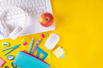 Back to school, online education high-colored bright yellow background. White laptop with school education supplies, headphones, pencil case and accessories top view flat lay copy space