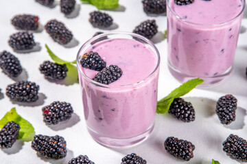 Two glasses of blackberry smoothie, yogurt or milkshake with fresh berry, mint leaves on white table background copy space