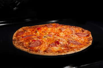 Burnt pizza with sausage, ham, mushroom, pepper, cheese on tray in electric oven, black background. Italian cuisine, failure, problem, fast food concept