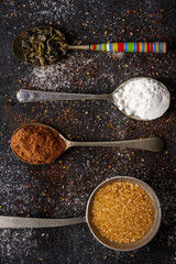 Spoons with green tea, cocoa, icing and cane sugar on black background sprinkled with sugar,...